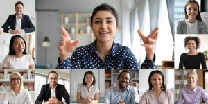 Composite photo of multiple people on a web conference. The middle person is a young woman in a blue collared shirt, using hand gestures. There are 10 small images of a diverse range of her colleagues