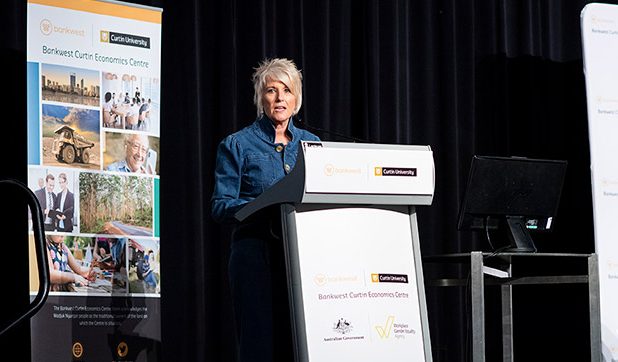 Libby Lyons talking on stage at a lectern with a BCEC pull up banner behind her